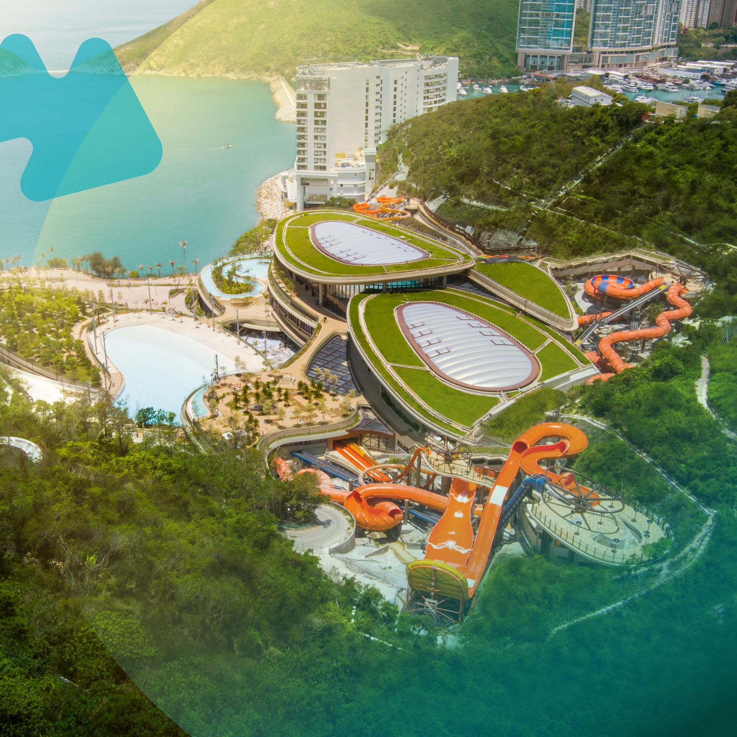 Aerial view of Ocean Park Hong Kong's Water World attraction featuring multiple water slides, parks, and buildings surrounded by lush greenery and urban high-rise buildings in the background.